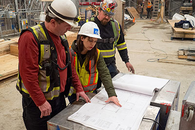 UBC student looking at blueprints at a construction site with two colleagues