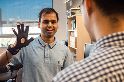 A graduate student showing a colleague how his speech synthesis wearable device prototype works