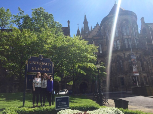 Three women smiling in front of a University of Glasgow sign