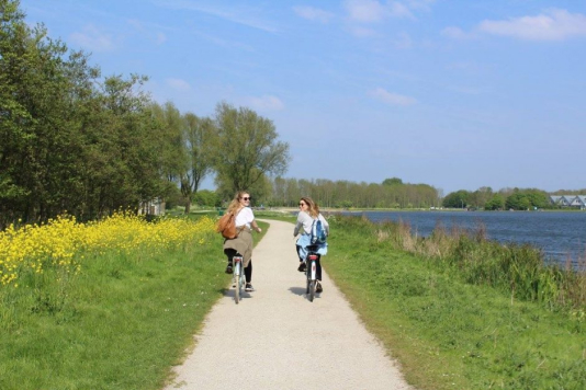 Two women riding bikes along a riverbank in the Netherlands