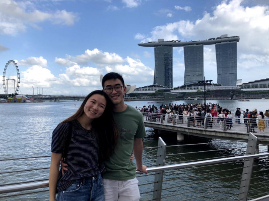 Tony and his partner smiling with the Singapore coastline behind them