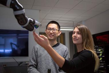 Two graduate students interacting with a robotic arm