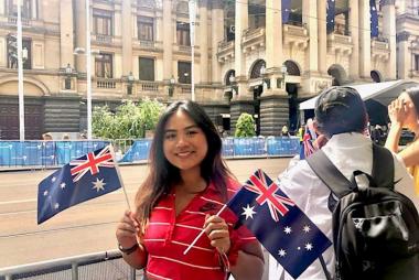 Student on exchange holding two Australian flags on the side of a street during a parade.