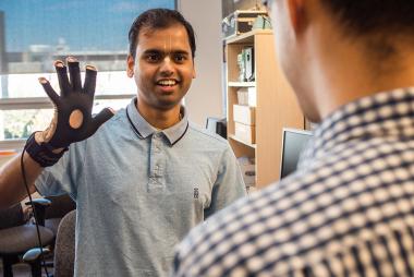 A graduate student showing a colleague how his speech synthesis wearable device prototype works