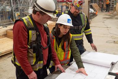 UBC student looking at blueprints at a construction site with two colleagues