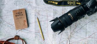 A Nikon camera, pencil, notebook, and backpack on top of a map.