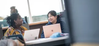 2 female-presenting students sit at table with laptops